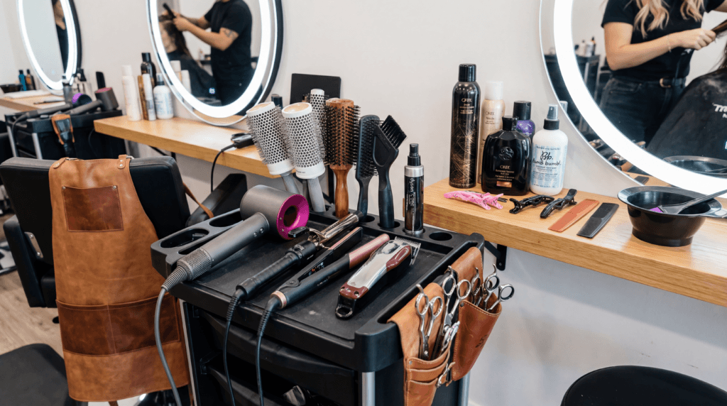 Professional hairstyling station with flat irons, curling irons, hair dryer, clippers, styling chair, hair clips and a color bowl, and combs.